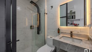 Une salle de bain moderne avec une douche à parois de verre, des toilettes blanches et un meuble-lavabo en marbre agrémenté d’un miroir.