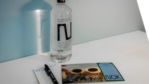 Une bouteille d’eau transparente avec le texte « REPRENNEZ VOTRE PLACE, ÉCRIREZ VOTRE HISTOIRE » et un stylo posés sur une surface blanche.