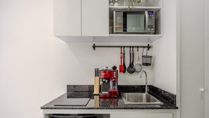 Une cuisine compacte équipée d’un four à micro-ondes, d’une machine à café et d’ustensiles suspendus.