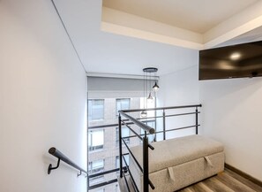 A modern apartment with a bunk bed, a mounted TV, and a view of the city through large windows.