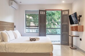 A modern hotel room with a large bed, a TV mounted on the wall, and a balcony with a view of the city.