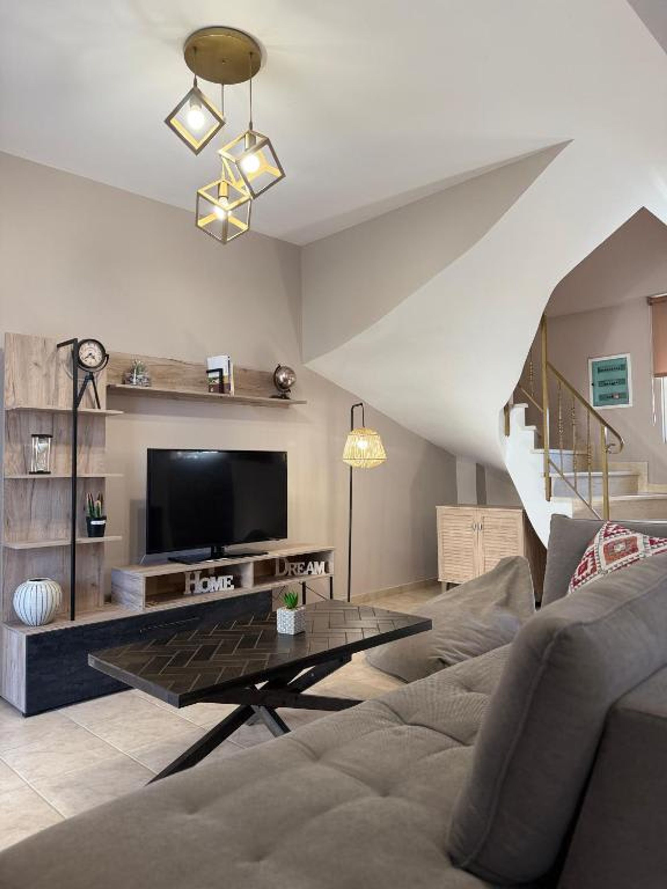 A modern living room with a flat-screen TV, a coffee table, and a sofa. There is a staircase leading to an upper level.