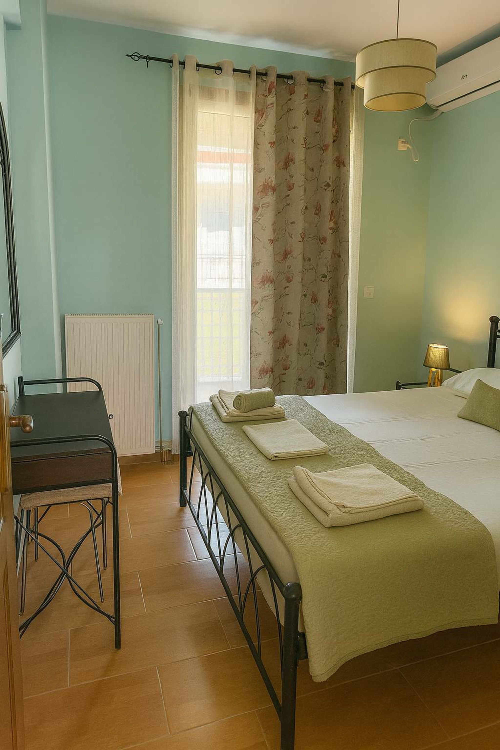 Un dormitorio con cama, escritorio, silla, radiador y ventana con cortinas.