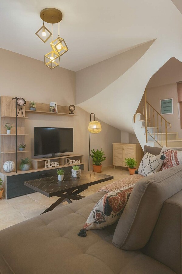 A modern living room with a flat-screen TV, a coffee table, and a sofa. There are decorative items on shelves and a staircase in the background. - Il Gusto Maisonette - Seaview Private Retreat (West Mani)