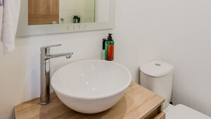A modern bathroom with a wooden vanity, a white sink, a mirror, and a toilet. - NOK Perfect Loft in Chic (Bogotá)