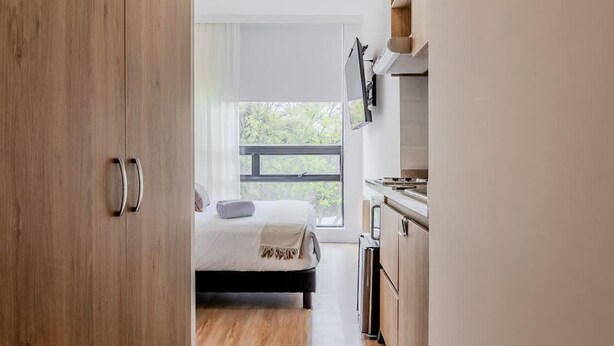 A modern bedroom with a large window, a bed, and a kitchenette. - NOK Perfect Loft in Chic (Bogotá)