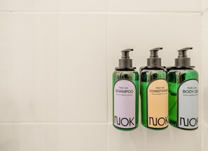 Three bottles of NUK hair and body care products on a white tiled wall.