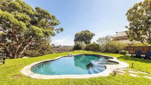 Piscina com borda de pedra, rodeada por gramado bem cuidado e árvores.