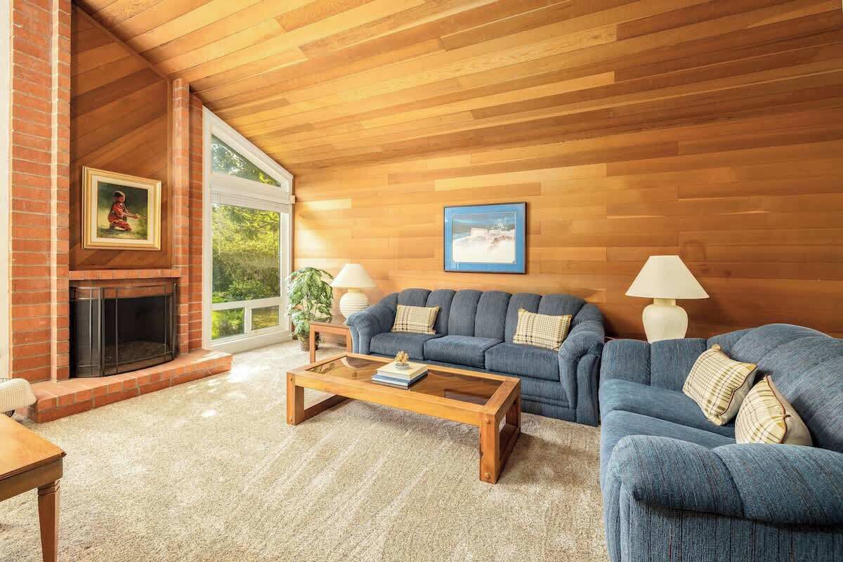 A living room with a fireplace, blue sofa, wooden coffee table, and a large window.