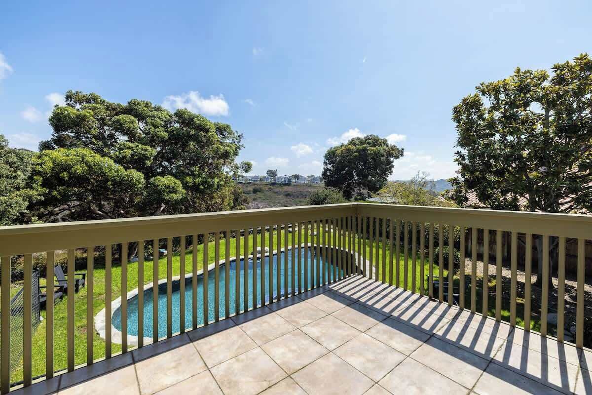 Un balcón con vista a una piscina, rodeado de árboles y un cielo despejado.