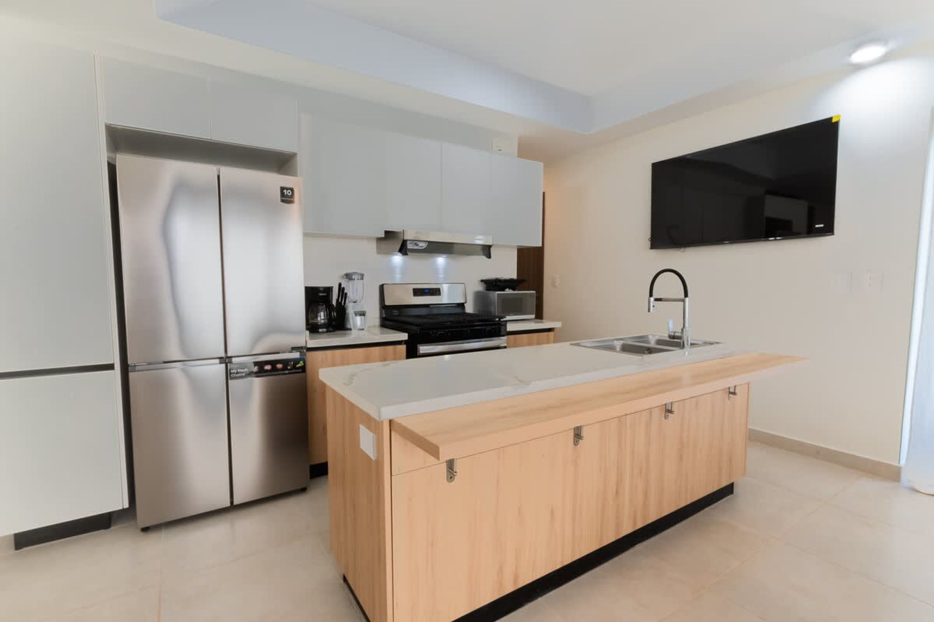 Una cocina moderna con un refrigerador de acero inoxidable, horno empotrado, microondas y un lavabo.