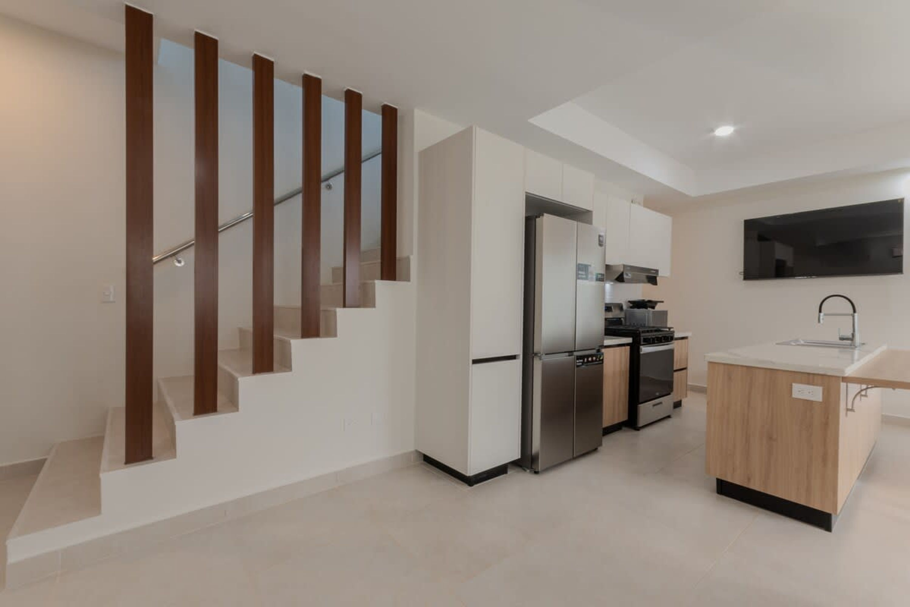 A modern kitchen with a built-in refrigerator, oven, and microwave. There is a wooden staircase with glass railings leading to an upper level.