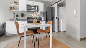 Eine moderne Küche mit weißen Schränken, einem Edelstahl-Kühlschrank und einem Essbereich mit weißem Tisch und Korbstühlen.