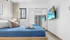 Ein Hotelzimmer mit Bett, Flachbildfernseher, Deckenventilator und Meerblick durch ein Fenster.