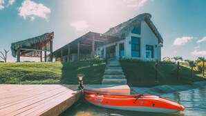 A house with a thatched roof, a wooden dock, and a red kayak.