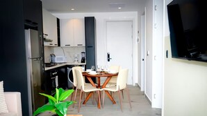 A modern kitchen with white cabinets, a dining area with a wooden table and chairs, and a TV mounted on the wall.