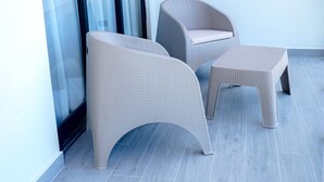 Ein Balkon mit zwei Korbstühlen, einem kleinen Tisch und einer Schiebetür. Eine weiße Wand ist ebenfalls zu sehen.