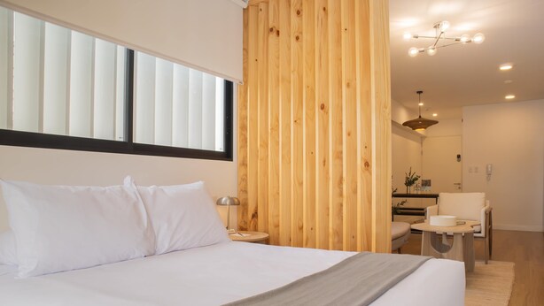 Un dormitorio moderno con una cama grande, panel de pared de madera y una pequeña zona de escritorio.