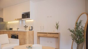 Cocina moderna con armarios blancos, microondas y encimeras de madera. Se observa un comedor con mesa y sofá. También hay un espejo y una planta en maceta.
