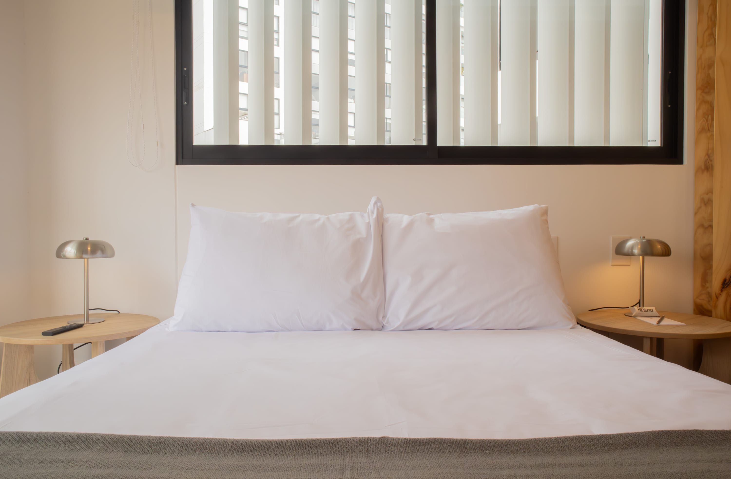 Ein Hotelzimmer mit einem großen Bett, zwei Nachttischen inklusive Lampen und einem Fenster mit Jalousien.