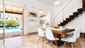 A modern dining area with a wooden table and white chairs, a staircase, and a view of a swimming pool. - Bouganvilla House FOR 6 PERSONS (Ariany)