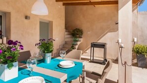 An outdoor dining area with a table set for two, a hanging light fixture, and a staircase leading to an upper level. - Bouganvilla House FOR 6 PERSONS (Ariany)