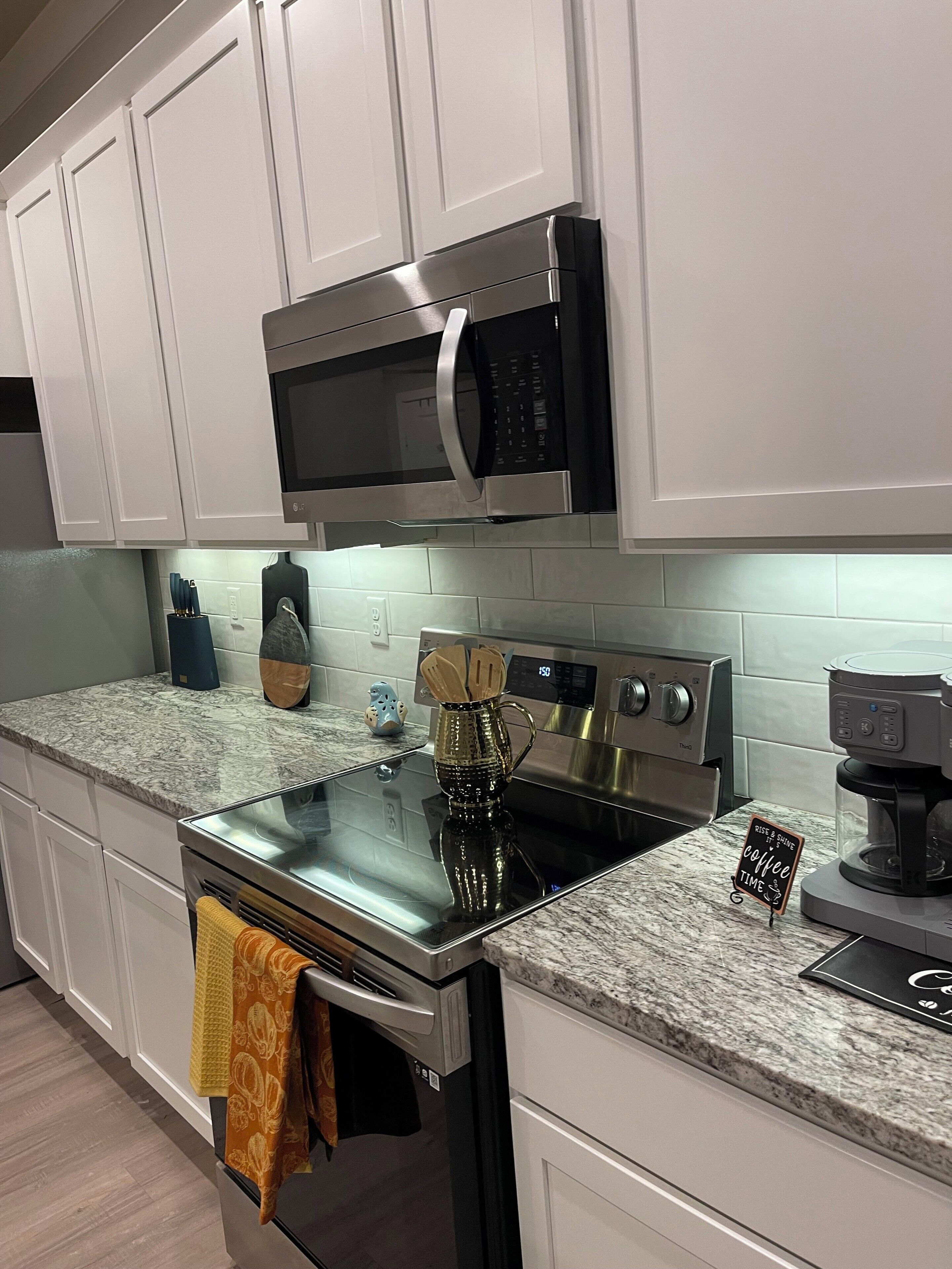 Una cocina moderna con armarios blancos, horno de acero inoxidable, microondas y cafetera.