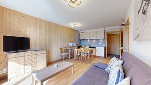 A modern living room with a flat-screen TV, wooden furniture, a sofa, and a dining area with a table and chairs.