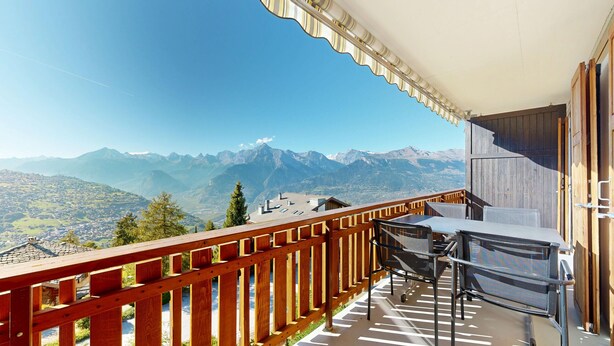 A balcony with a wooden railing overlooking a mountain view.