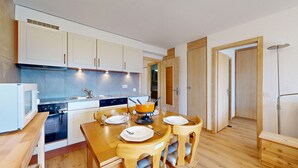 A compact kitchen with white cabinets, a built-in oven, and a dining area with a wooden table and chairs.