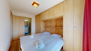 A bedroom with two beds, wooden paneling, a shower, and a red curtain.