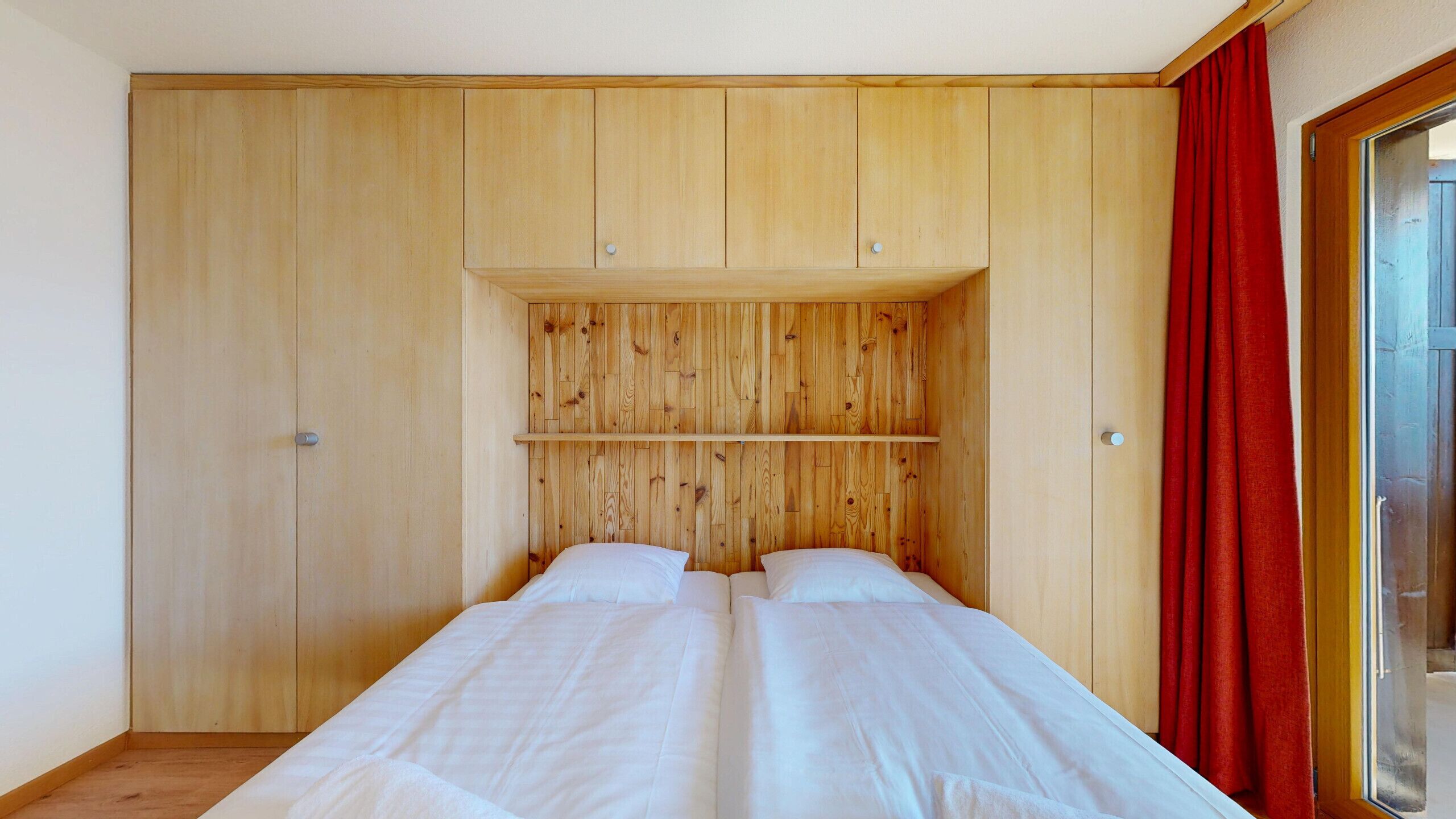 Ein Schlafzimmer mit einem Holzschrank, einem Bett mit weißer Bettwäsche und einem roten Vorhang.