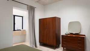 A bedroom with a bed, a wooden wardrobe, a dresser, and a mirror.
