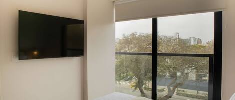 Un dormitorio moderno con un gran ventanal, un televisor de pantalla plana montado en la pared y una cama bien tendida.