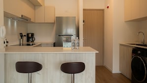 Cocina moderna con una isla central, dos taburetes de bar, un refrigerador de acero inoxidable, una cafetera y una lavadora.