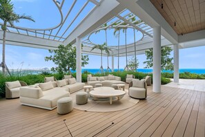 A covered outdoor seating area with a wooden deck, white furniture, and a view of the ocean. - NOK Fantastic 1 BR Den in Miami (Miami Beach)