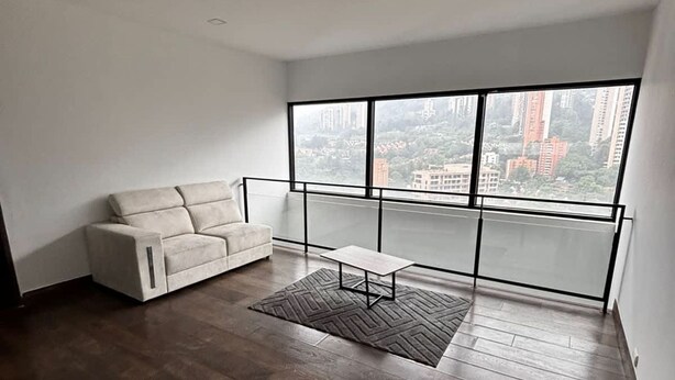 A spacious room with a large window, a white sofa, and a small table. - NOK Perfect Duplex in El Poblado (Medellín)