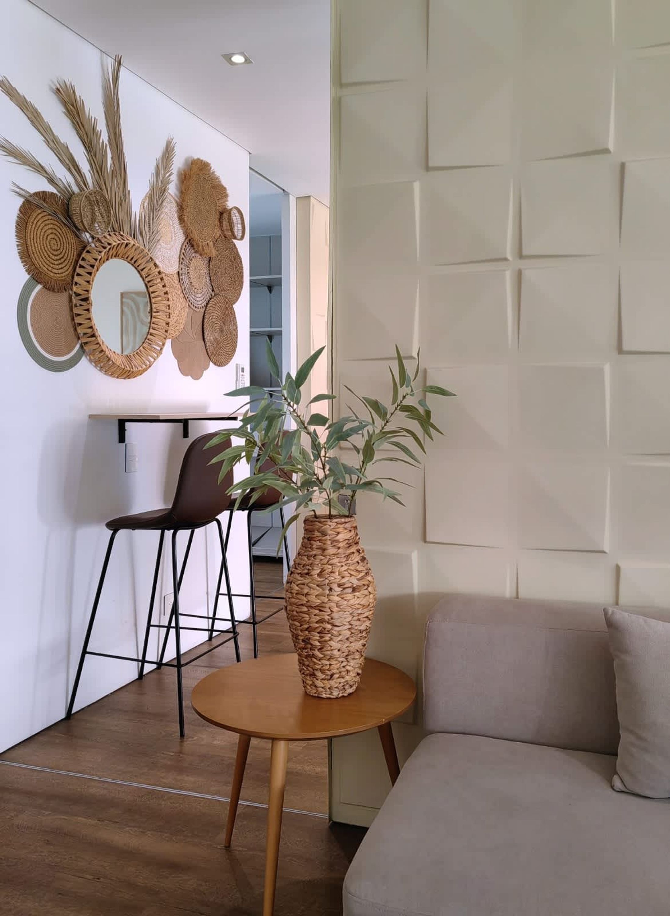 Una sala de estar moderna con una mesa redonda de madera, un jarrón tejido marrón con una planta, un sillón de cuero marrón y un sofá color beige.