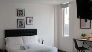 A modern bedroom with a large bed, a desk, and a chair. There are framed pictures on the wall and a window with a view. - NOK Beatiful Loft in Chic (Bogotá)