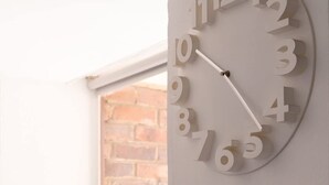A wall-mounted clock with numbers and hands, a potted plant, and a brick wall in the background. - NOK Beatiful Loft in Chic (Bogotá)