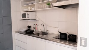 A modern kitchen with white cabinetry, a stainless steel countertop, a microwave, a coffee maker, a sink with a faucet, and a few pots and pans. - NOK Beatiful Loft in Chic (Bogotá)