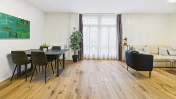 Ein modernes Wohnzimmer mit Essbereich, mit Holzboden, einer Couch, einem Couchtisch und einem Esstisch mit Stühlen.