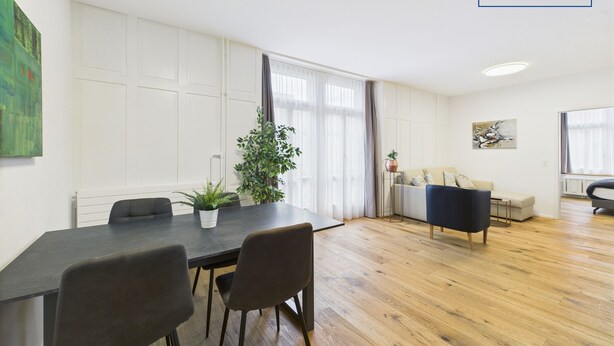 Una sala de estar moderna con comedor, suelo de madera y un ventanal con cortinas.