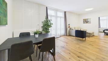 Una sala de estar moderna con comedor, suelo de madera y un ventanal con cortinas.