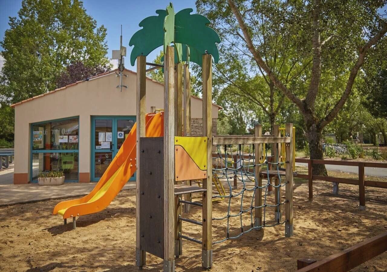 A playground with a slide, climbing structures, and a building with a window and a sign.