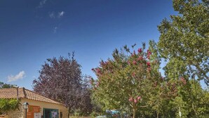 A building with a tiled roof and a green door, surrounded by trees and shrubs. - Camping Marvilla Parks - Clos Cottet (Angles)