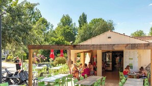 An outdoor cafe with tables and chairs, surrounded by greenery and trees. - Camping Marvilla Parks - Clos Cottet (Angles)