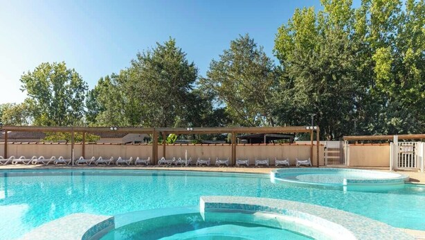 A swimming pool with a hot tub, lounge chairs, and a covered area with trees in the background. - Camping Marvilla Parks - Clos Cottet (Angles)