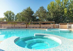 A swimming pool with a hot tub, lounge chairs, and a covered area with trees in the background. - Camping Marvilla Parks - Clos Cottet (Angles)