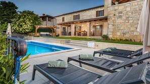 Un espace aménagé au bord de la piscine, avec des chaises longues et un bâtiment en pierre doté d’un balcon.